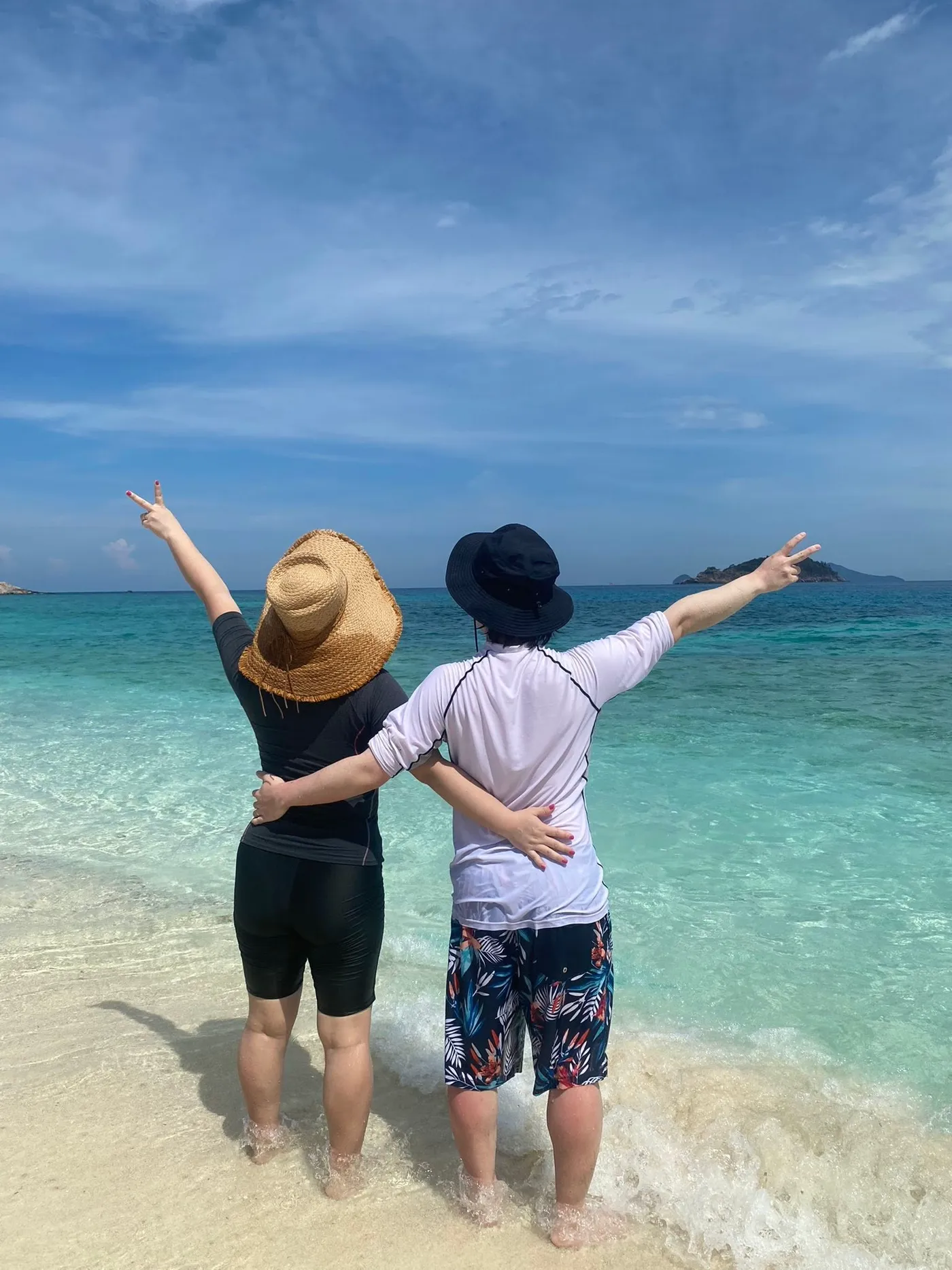Two friends throwing peace signs on the beach in front of bright, shallow turquoise water
