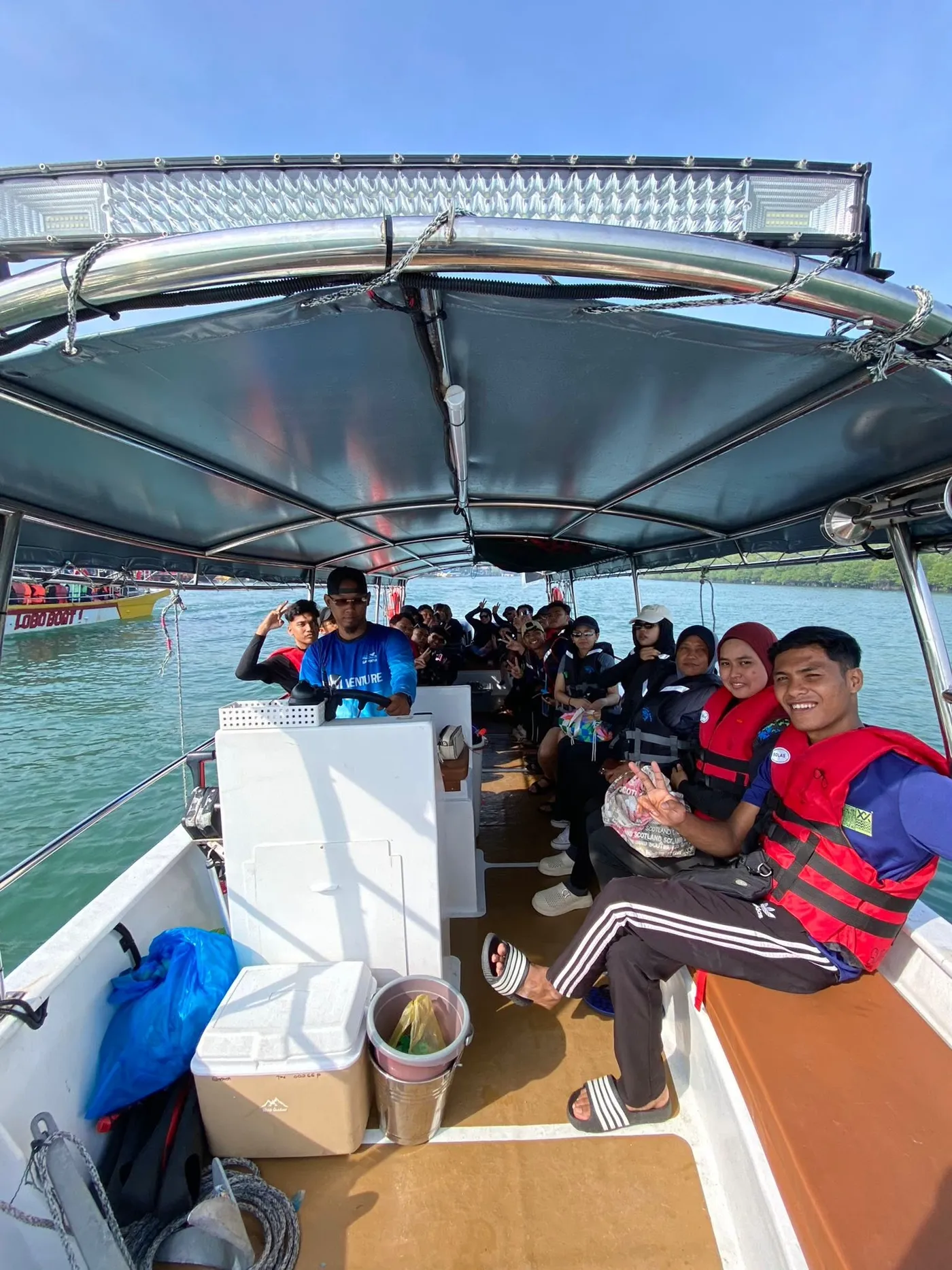 Our captain steering the boat from the helm, with guests in red life jackets smiling and giving peace signs behind him