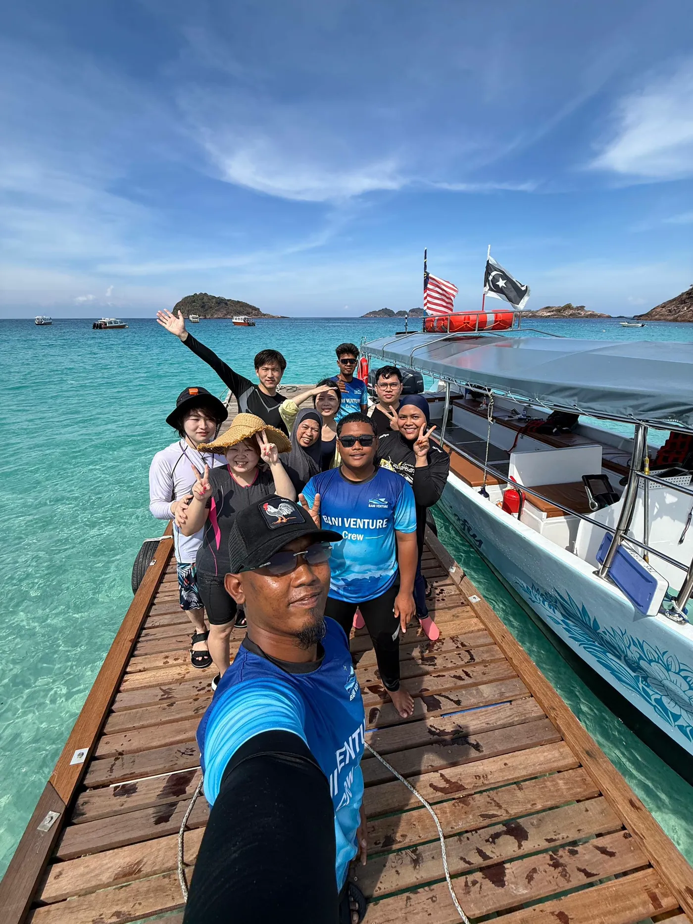 Guests and crew smiling together on the wooden jetty with turquoise water and the Suraya boat behind them